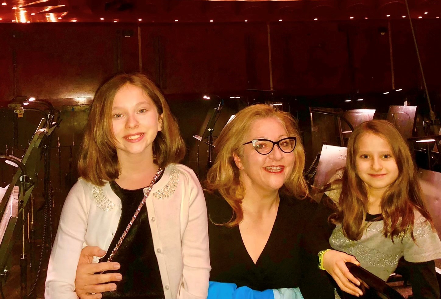 A woman smiles with her two daughters. They are in a theater. 
