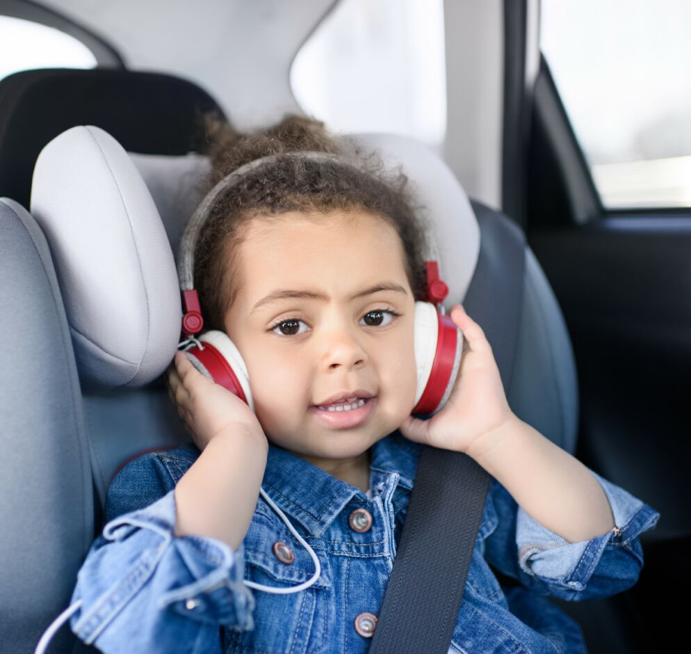 A child sitting in a car seat has headphones on. 
