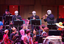 Three people in alien costumes play instruments in an orchestra