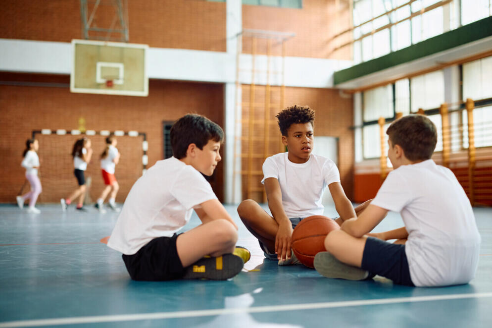 Group of elementary students talking while sitting on the floor during physical education class at school. 