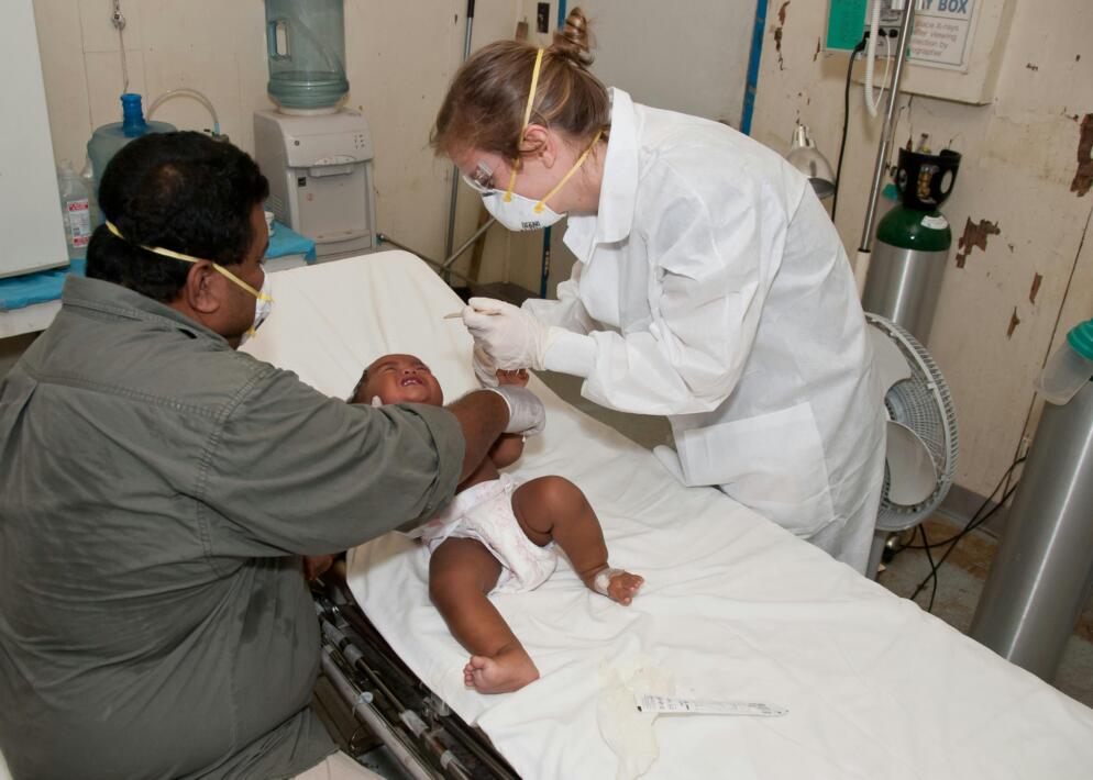 A baby lying on a hospital bed receives a checkup from the doctor