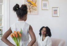 A girl holds flowers behind her back to give her mother