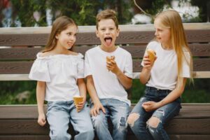 Three kids sitting on a bench and eating ice cream