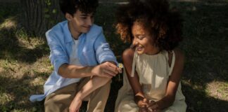 A teenage boy and girl sitting under a tree. The boy is giving the girl a flower.
