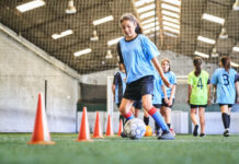 Empowering Parents in Recognition of Safe Sport Day Young girl leading ball between cones on sports court. Female player in blue jersey practicing dribbling skill at court.